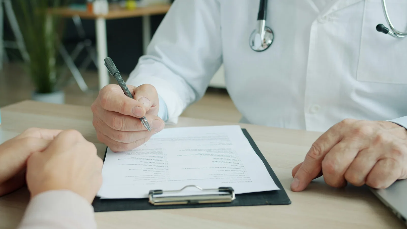 Doctor writing on a clipboard across the desk from another person