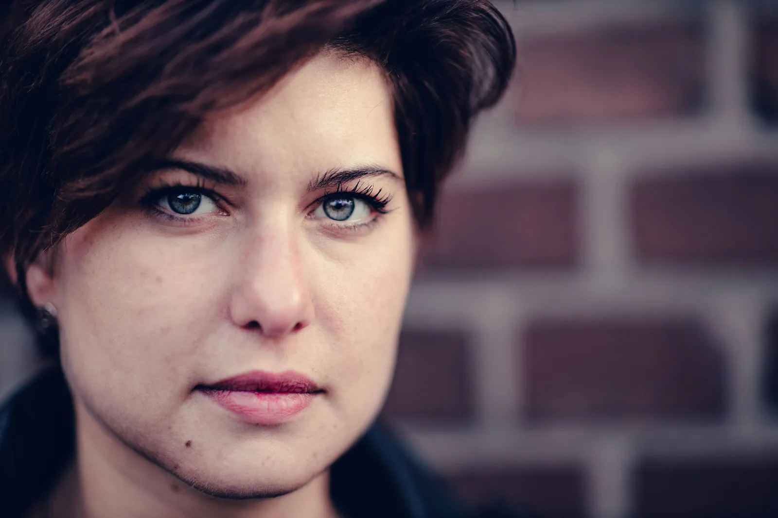 Portrait of a woman with short dark hair beside a brick wall