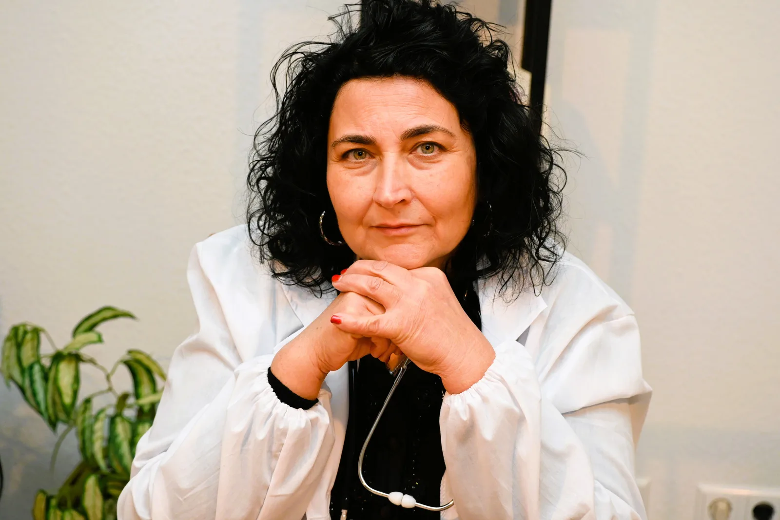 Doctor wearing a white coat and stethoscope, seated with hands clasped