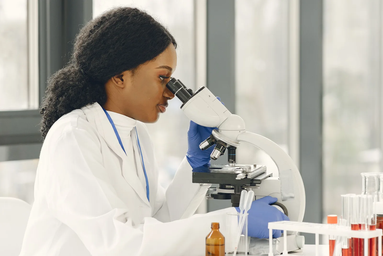 Laboratory professional looking through a microscope beside sample tubes