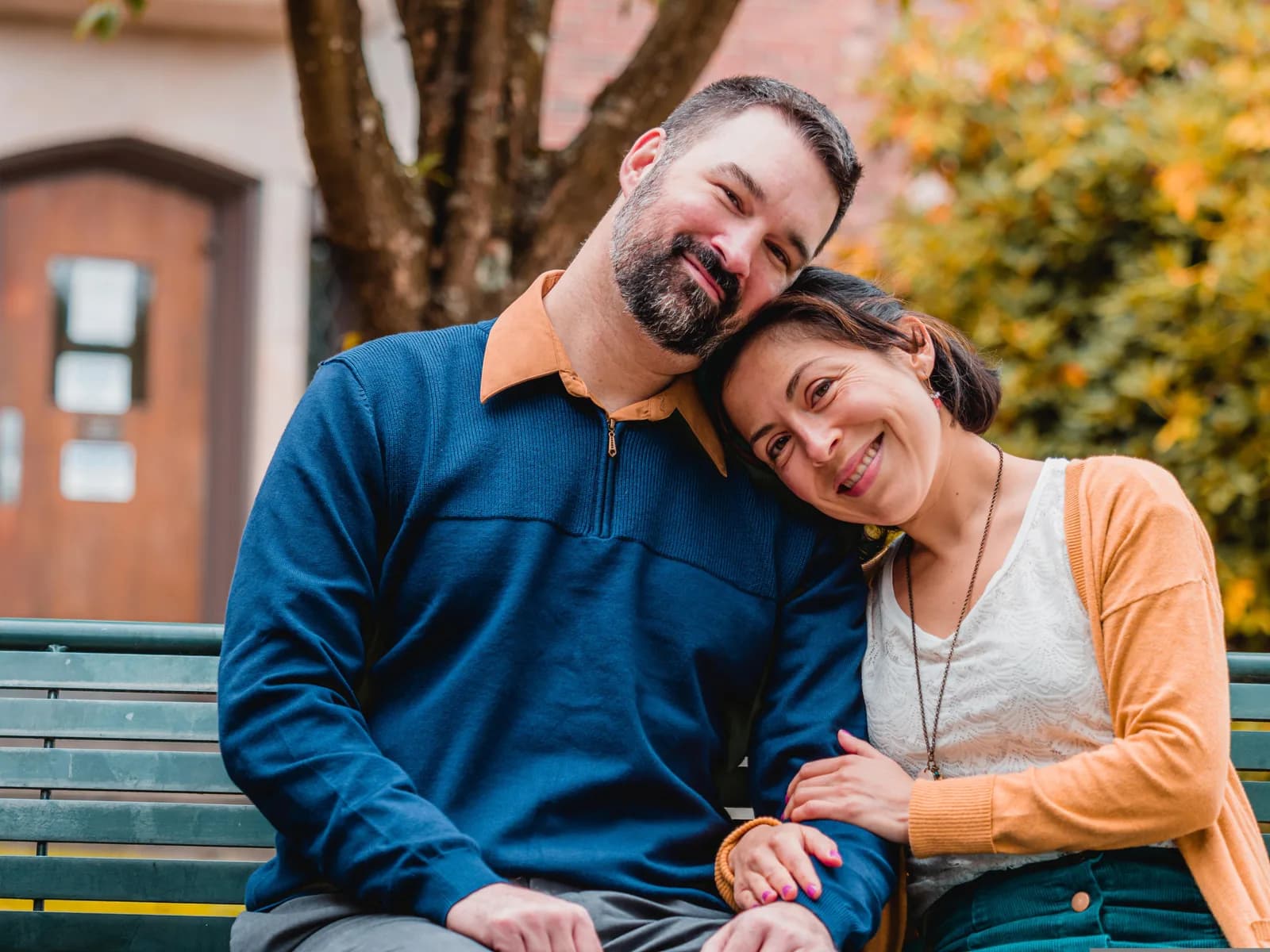 Two people sitting close together on a park bench with their heads resting together