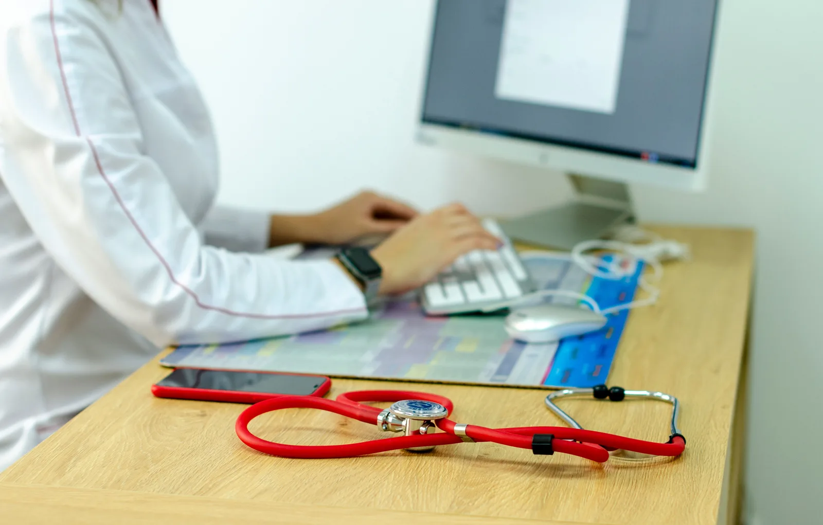 Clinician using a computer with a red stethoscope on the desk