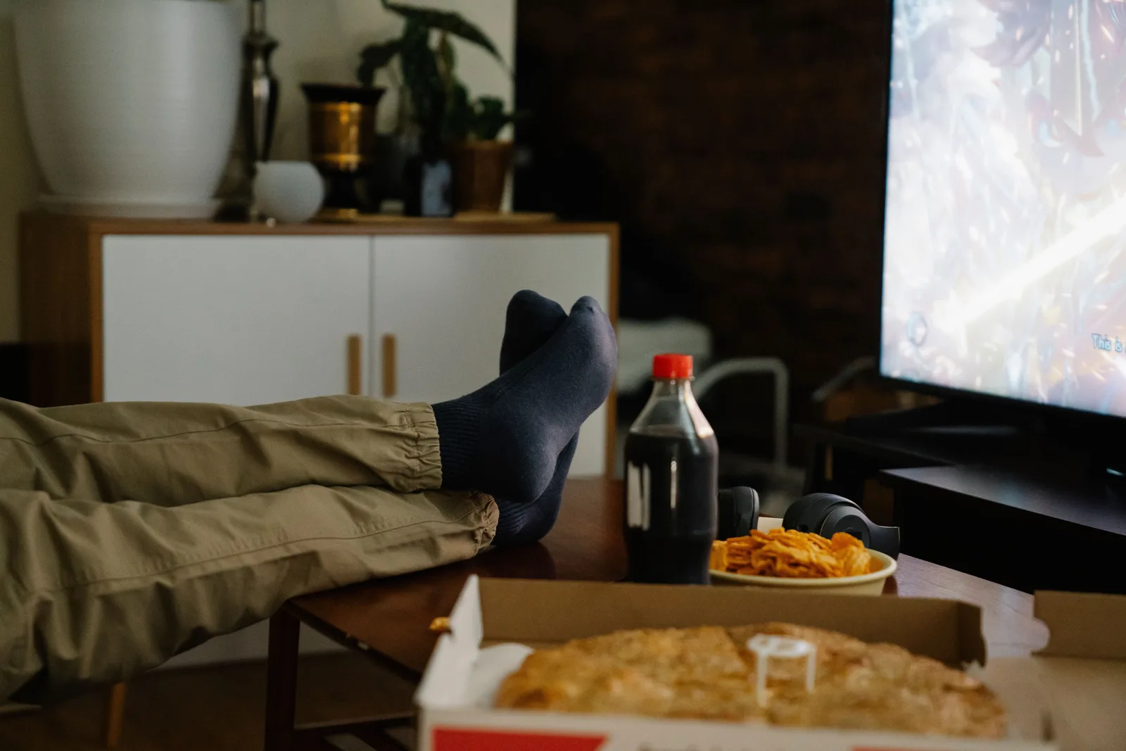Person reclining on a couch near snack food and a sugary drink